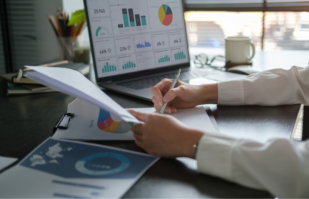 Photograph of a self-employed solopreneur working on a stack of self-employment business documents on a desk in front of a computer.